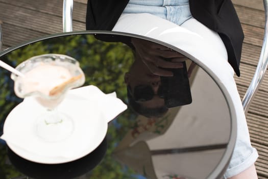 reflection on the table of a business woman in sunglasses eats her favorite delicious ice cream, dressed in a black elegant jacket, her tablet lies on the table, she enjoys a break from work