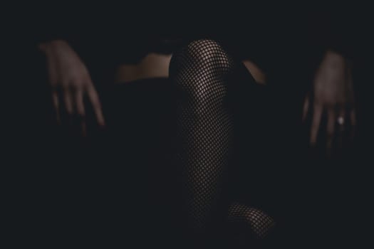 slim sexy woman in black stockings sits on a chair on a black background