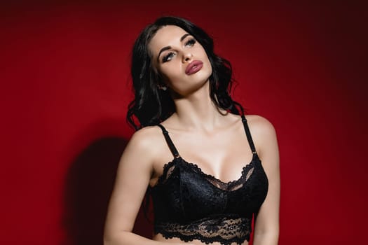 Sexy woman in lace black sensual lingerie with long curly hair posing on red background in studio.