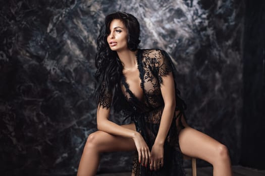 Sexy woman in lace black sensual robe with long curly hair posing in studio.
