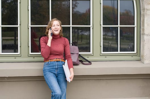 a young caucasian girl returns to college, stands with a backpack and notebooks and talks on the phone in a laugh, back to school, High quality photo