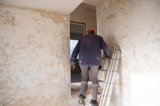 a male builder stands in an apartment near peeling walls and starts repairs in a new house in the middle of an empty room, High quality photo