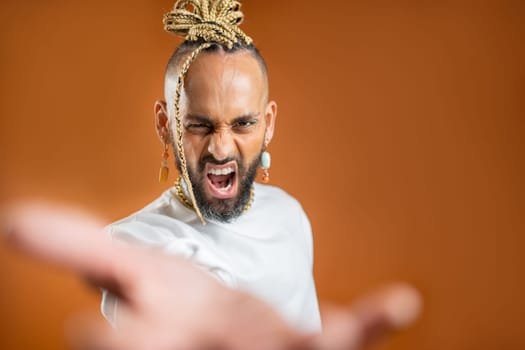 African-american gay with bright make up reaching empty open palm hand toward to camera and scream loud. Mock up advertisement concept. Homosexual serious man outstretching empty hand towards camera.