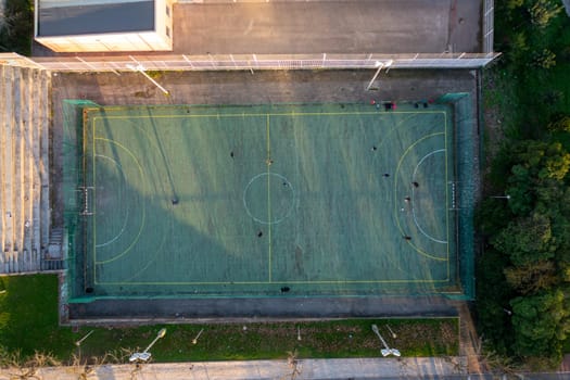 Aerial drone top view of mini football soccer field with artificial plastic cover with playing people. Public sport ground in city at sunny summer day drone view