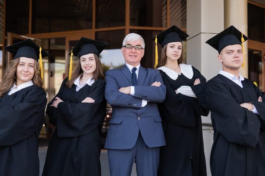 A professor and his students in graduation gowns stand with their arms crossed over their chests