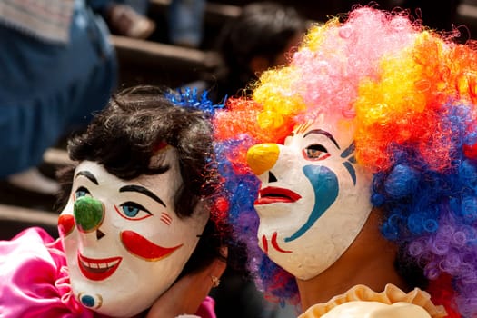 two people in a carnival in latin america with handmade masks. people also have wigs