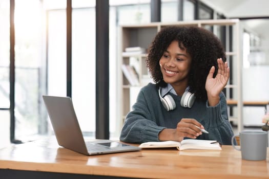 Smiling young african american teen girl wear headphones video calling on laptop. Happy woman student looking at computer screen watching webinar or doing video chat by webcam..