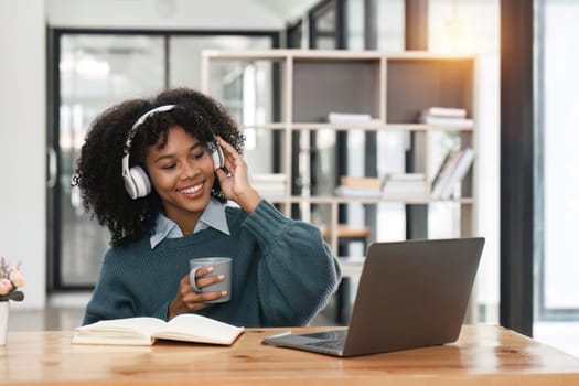 Smiling young african american teen girl wear headphones video calling on laptop. Happy woman student looking at computer screen watching webinar or doing video chat by webcam..