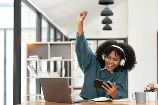 Excited african american in headphone hold smartphone feel euphoric reading good news, overjoyed happy black biracial young woman use cellphone triumph win online gaming.
