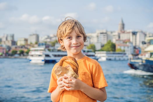 Boy in Istanbul having breakfast with Simit and a glass of Turkish tea. Glass of Turkish tea and bagel Simit against golden horn bay and the Galata Tower in Istanbul, Turkey. Turkiye. Traveling with kids concept.