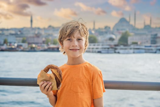 Boy in Istanbul having breakfast with Simit and a glass of Turkish tea. Glass of Turkish tea and bagel Simit against golden horn bay in Istanbul, Turkey. Turkiye. Traveling with kids concept.