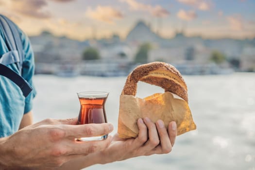 Man in Istanbul having breakfast with Simit and a glass of Turkish tea. Glass of Turkish tea and bagel Simit against golden horn bay in Istanbul, Turkey. Turkiye.