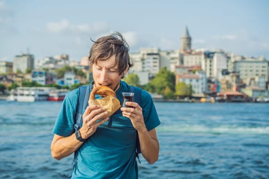 Man in Istanbul having breakfast with Simit and a glass of Turkish tea. Glass of Turkish tea and bagel Simit against golden horn bay and the Galata Tower in Istanbul, Turkey. Turkiye.