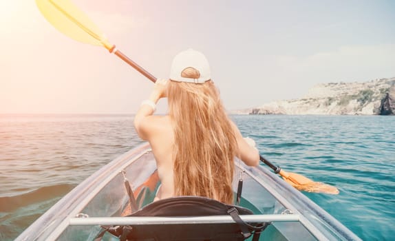 Woman in kayak back view. Happy young woman with long hair floating in transparent kayak on the crystal clear sea. Summer holiday vacation and cheerful female people having fun on the boat.