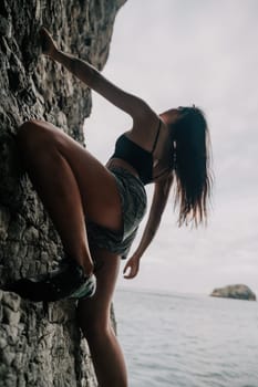 A girl climbs a rock. The athlete trains in nature. Woman overcomes difficult climbing route. Extreme hobby. Tourist woman rock climber hiking on mountains rocks over beautiful sea coast