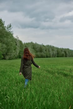 a woman in a long raincoat runs across a field in tall green grass in cloudy weather in spring. High quality photo