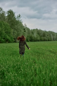 a woman in a long raincoat runs across a field in tall green grass in cloudy weather in spring. High quality photo