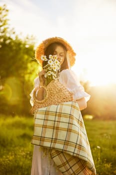 portrait of a happily smiling woman in a field lit from the back by the rays of the setting sun with a basket of flowers and a blanket in her hands. High quality photo