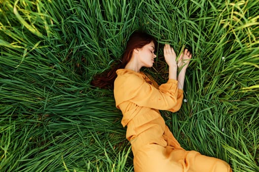 a relaxed woman enjoys summer lying in the tall green grass with her eyes closed. Photo taken from above. High quality photo