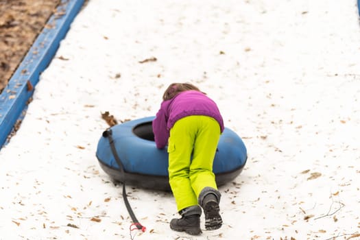 Little girl sliding downhill on tube.