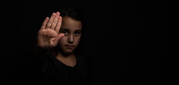 little girl with a raised hand making a stop sign gesture on a black background. Violence, harassment and child abuse prevention concept