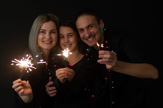 Young family with sparklers at Christmas time on a black background.