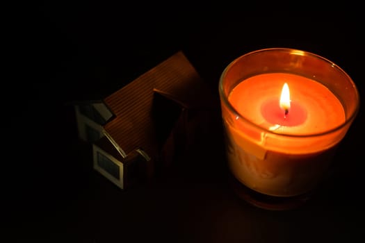 a candle and a toy house on dark background.