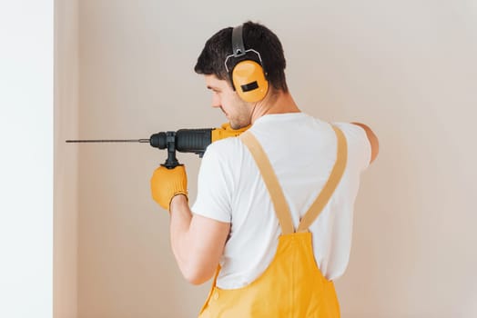 Handyman in yellow uniform works indoors by using hammer drill. House renovation conception.