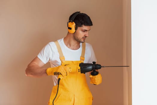 Handyman in yellow uniform works indoors by using hammer drill. House renovation conception.