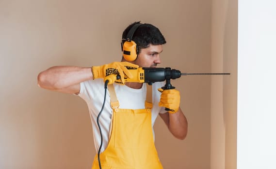 Handyman in yellow uniform works indoors by using hammer drill. House renovation conception.