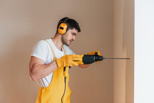 Handyman in yellow uniform works indoors by using hammer drill. House renovation conception.