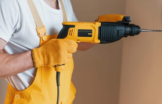 Handyman in yellow uniform works indoors by using hammer drill. House renovation conception.