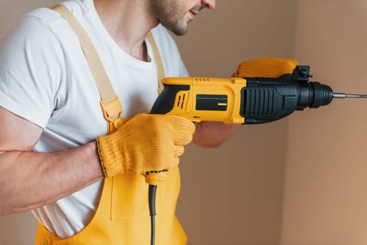 Handyman in yellow uniform works indoors by using hammer drill. House renovation conception.