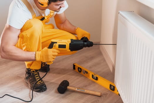 Handyman in yellow uniform works indoors by using hammer drill. House renovation conception.