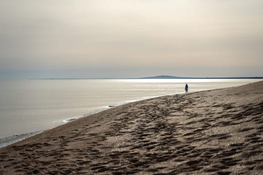 A slender woman in a beach dress walks along the seashore at sunset