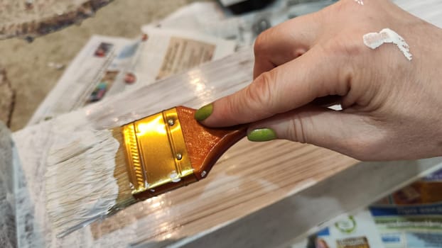 Woman hand painting on wooden boards with Brush full of white paint. Painting of new wood board or furniture and old newspaper on background. Partial focus