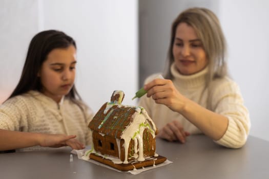 Mother and daughter making gingerbread cookies house, decorating at home, Christmas concept.