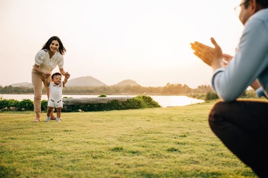 A young family enjoying a walk in the park on a sunny day, teaching their little one to take his first steps amidst the beauty of nature