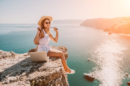 Digital nomad, Business woman working on laptop by the sea. Pretty lady typing on computer by the sea at sunset, makes a business transaction online from a distance. Freelance, remote work on vacation