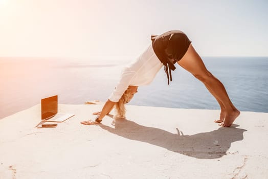 Happy girl doing yoga with laptop working at the beach. beautiful and calm business woman sitting with a laptop in a summer cafe in the lotus position meditating and relaxing. freelance girl remote work beach paradise