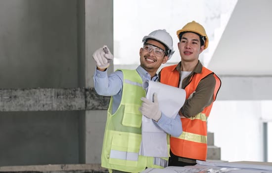 young man construction team engineer in vest and hat working with laptop standing on construction site House building project. Engineer talking with colleagues at work.