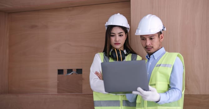 Structural engineer and architect dressed in reflective vests discuss the construction process by the chart and laptop...