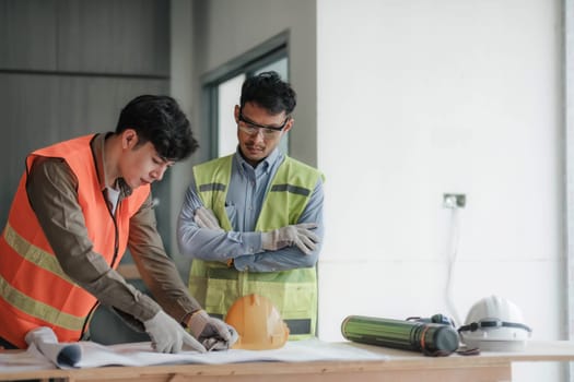 young man construction team engineer in vest and hat working with laptop standing on construction site House building project. Engineer talking with colleagues at work.