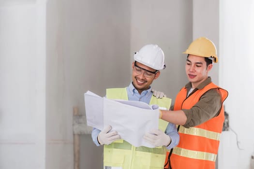 young man construction team engineer in vest and hat working with laptop standing on construction site House building project. Engineer talking with colleagues at work.