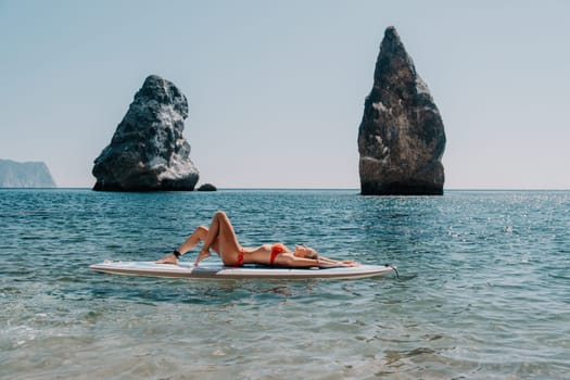 Close up shot of beautiful young caucasian woman with black hair and freckles looking at camera and smiling. Cute woman portrait in a pink bikini posing on a volcanic rock high above the sea