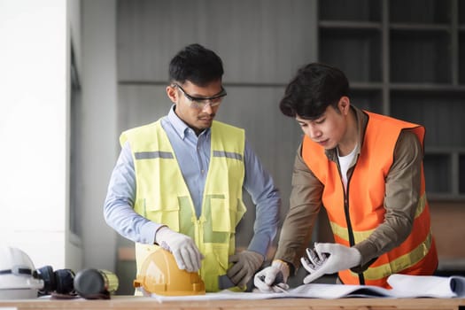 young man construction team engineer in vest and hat working with laptop standing on construction site House building project. Engineer talking with colleagues at work.