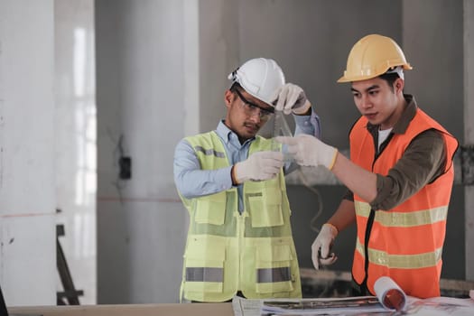 young man construction team engineer in vest and hat working with laptop standing on construction site House building project. Engineer talking with colleagues at work.