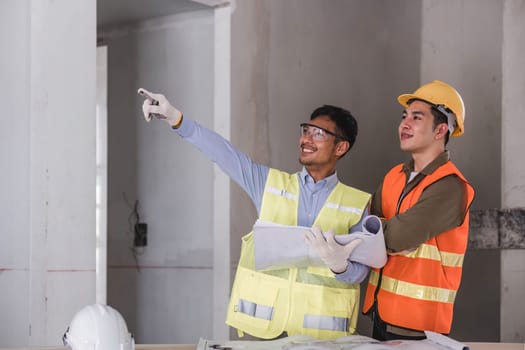 young man construction team engineer in vest and hat working with laptop standing on construction site House building project. Engineer talking with colleagues at work.