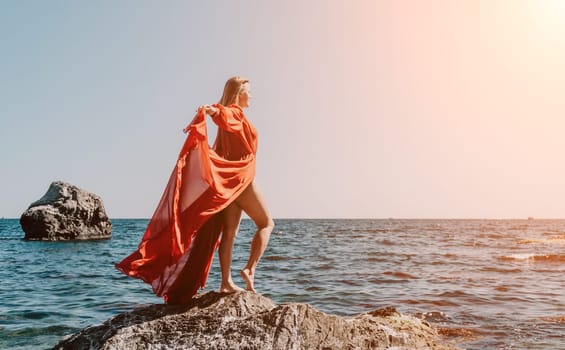 Woman travel sea. Young Happy woman in a long red dress posing on a beach near the sea on background of volcanic rocks, like in Iceland, sharing travel adventure journey