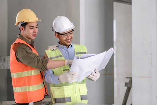 young man construction team engineer in vest and hat working with laptop standing on construction site House building project. Engineer talking with colleagues at work.